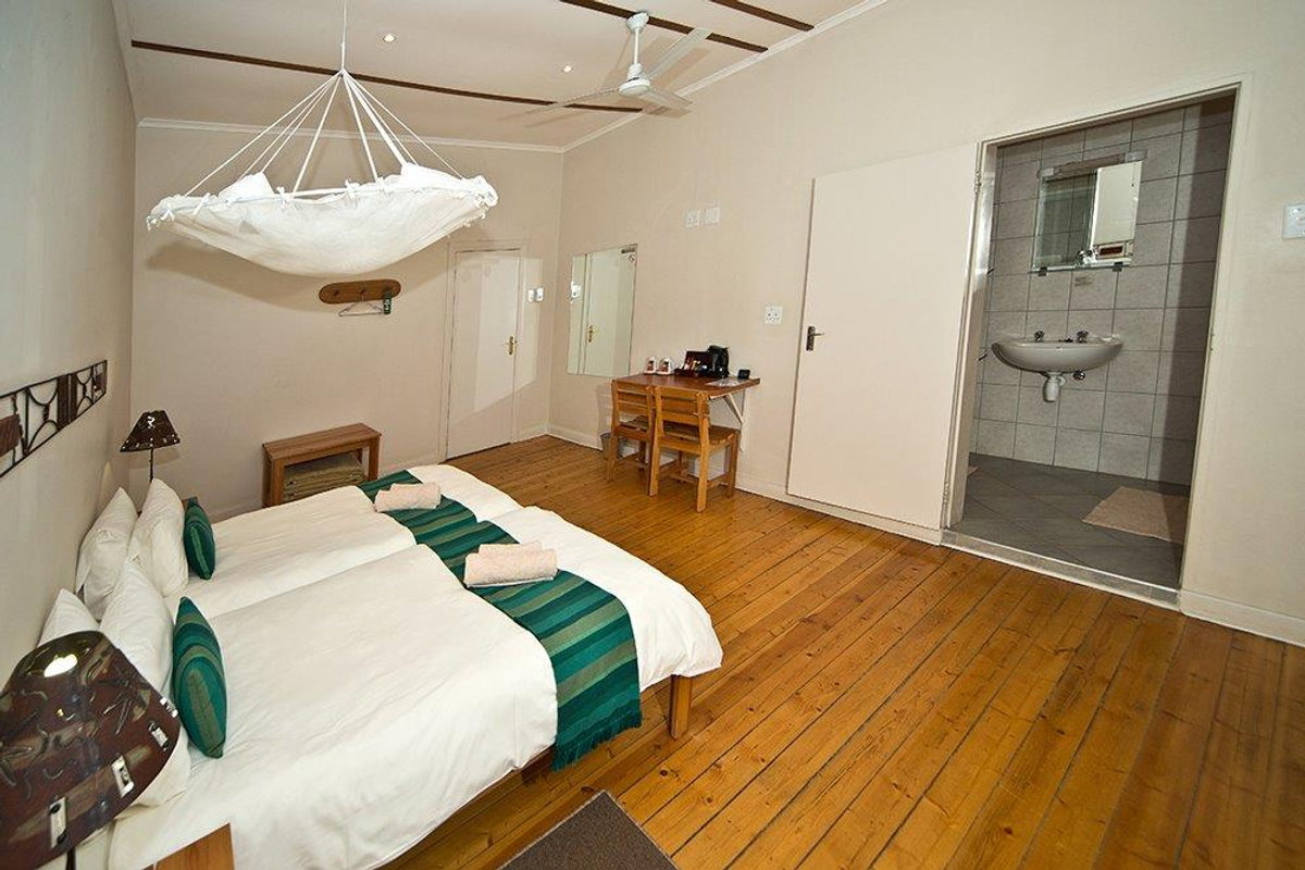 A hotel bedroom featuring polished wooden flooring, a ceiling fan, and an en-suite bathroom with tiled walls and a pedestal basin.