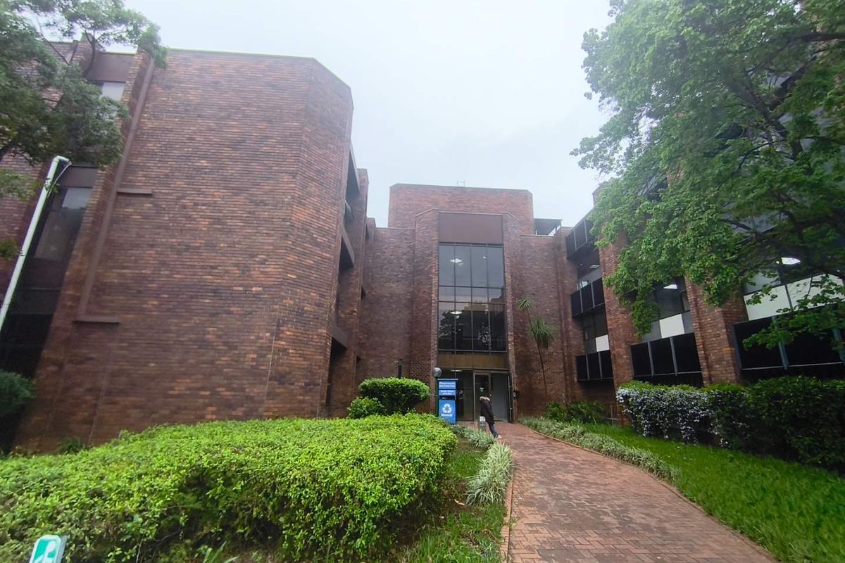 Front exterior view of a multi-story brick office building featuring a paved walkway, landscaped garden, and a prominent glass entrance.