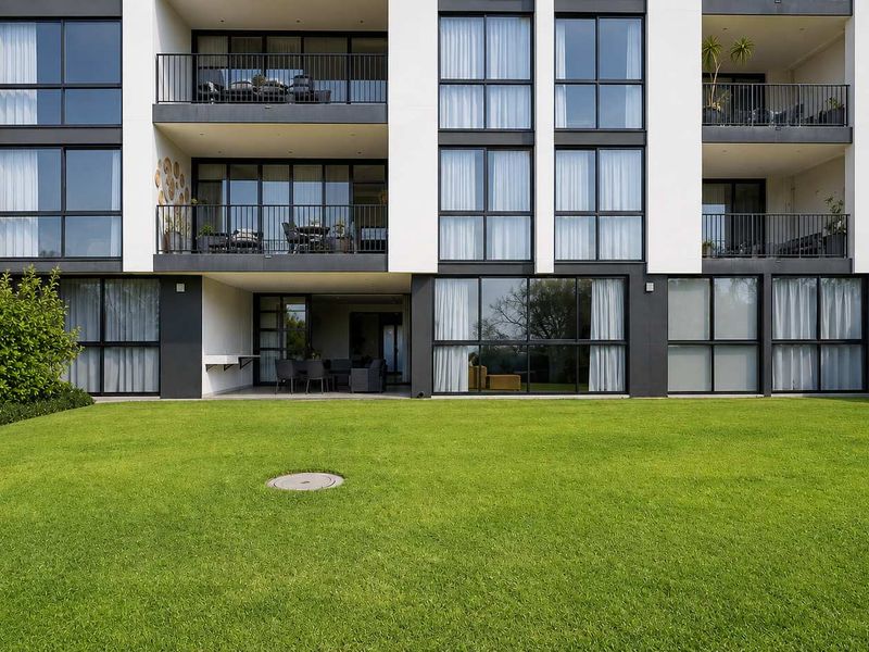 Rear view of a modern apartment building featuring private balconies, ground floor covered patio, and a well-maintained communal lawn area.