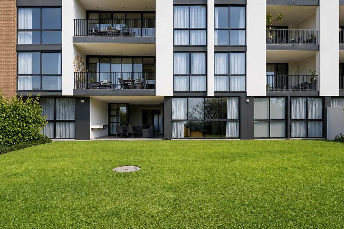 Rear view of a modern apartment building featuring private balconies, ground floor covered patio, and a well-maintained communal lawn area.