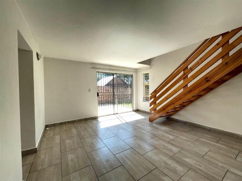 An open-plan living area featuring modern tiled flooring, a wooden staircase, and a sliding glass door leading to the exterior.