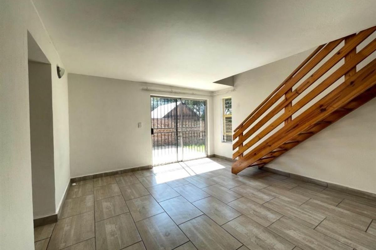 An open-plan living area featuring modern tiled flooring, a wooden staircase, and a sliding glass door leading to the exterior.