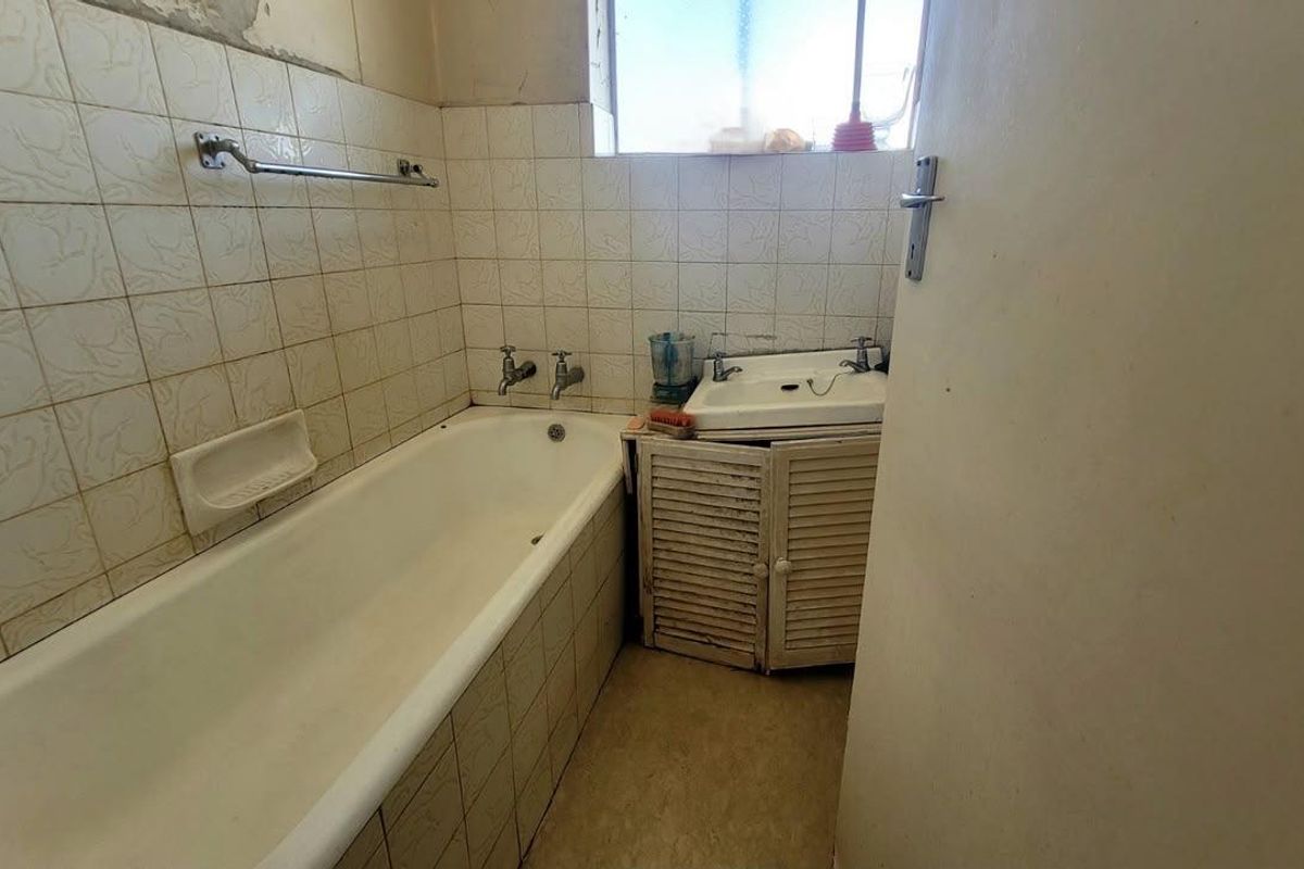A dated bathroom featuring a standard bathtub, wall-mounted basin, and tiled walls, requiring renovation to update the finishes and fixtures.