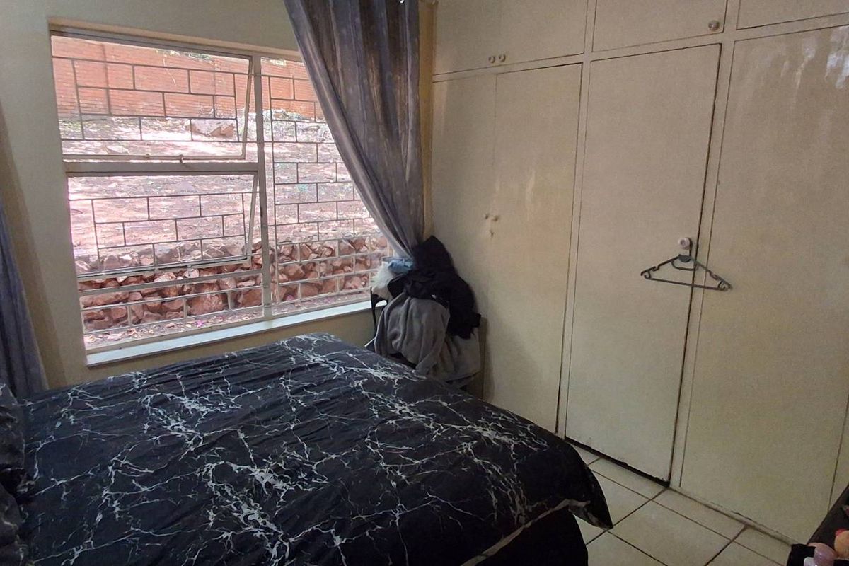 A bedroom featuring built-in cupboards with a tiled floor and a window overlooking the rear exterior area.