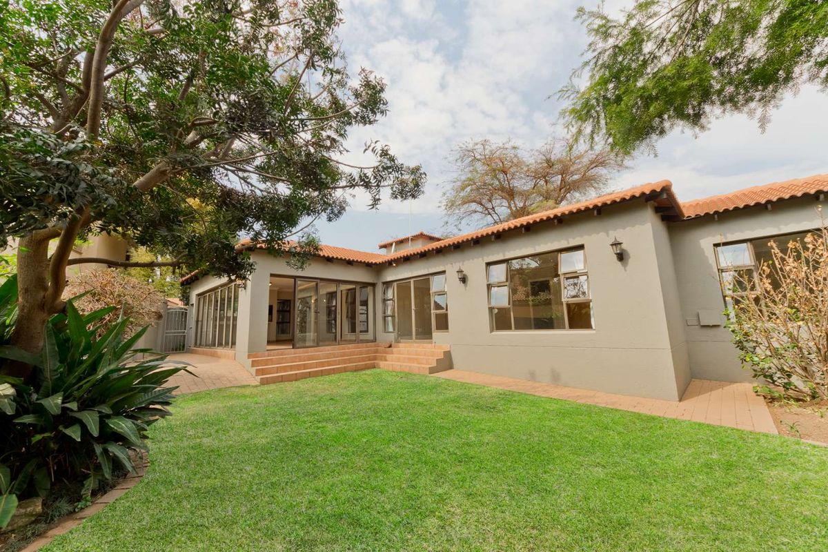 Rear view of the property featuring a well-maintained lawn, paved patio area, and large aluminium sliding doors providing access to the interior.