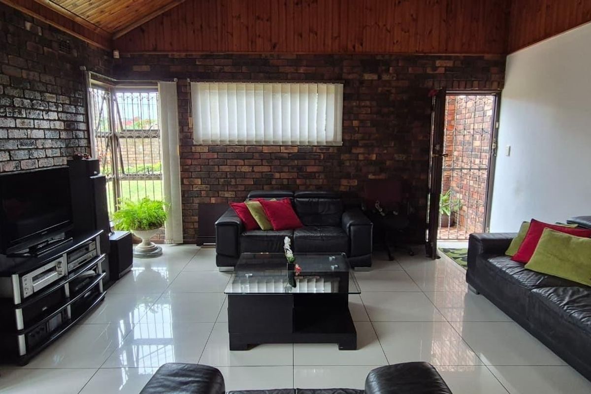 Spacious living room featuring exposed brick walls, a high timber vaulted ceiling, and polished floor tiles, with direct access to an outdoor area.