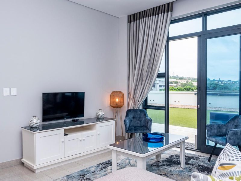 A bright living room featuring tiled floors and large sliding glass doors that provide seamless access to an outdoor balcony area.