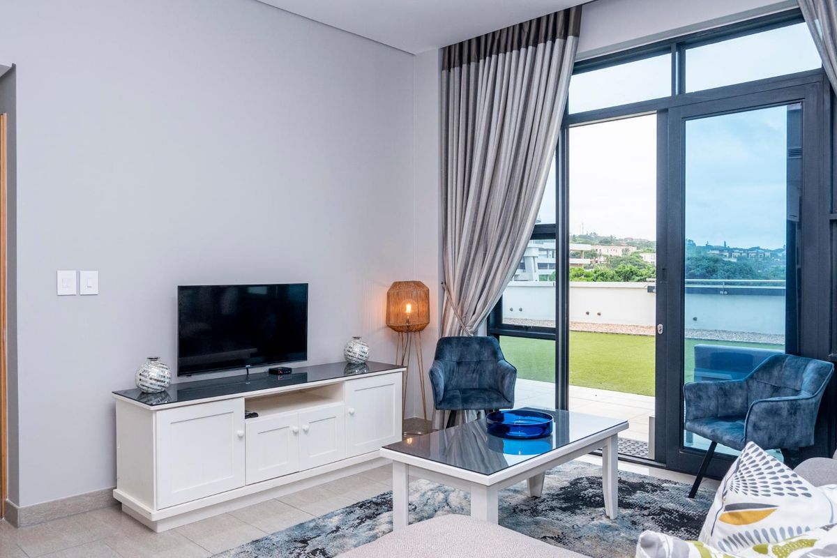 A bright living room featuring tiled floors and large sliding glass doors that provide seamless access to an outdoor balcony area.