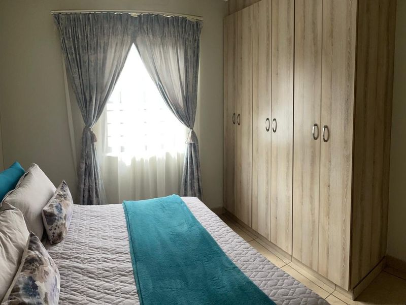 A well-maintained bedroom featuring light wood-finish built-in cupboards and neutral tiled flooring, offering ample storage space.