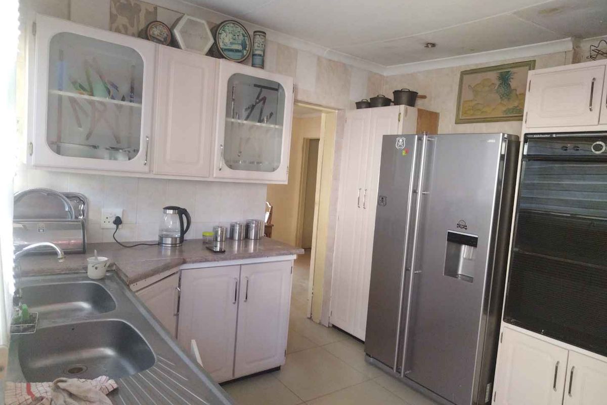 A dated kitchen featuring laminate countertops, double stainless steel sink, built-in oven, and ample cabinetry storage space.