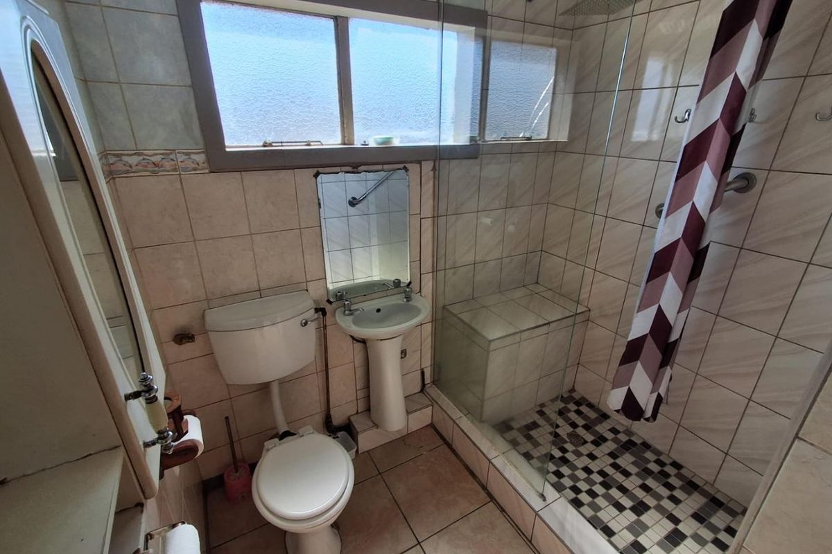 A compact bathroom featuring a walk-in shower with a built-in bench, pedestal basin, and toilet, requiring cosmetic updates to modernize the finishes.