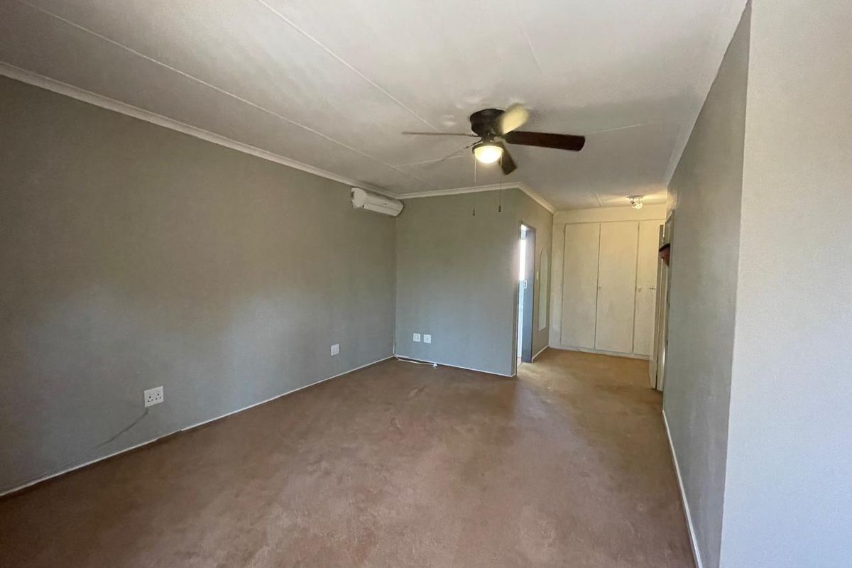 Spacious bedroom featuring built-in cupboards, a ceiling fan, and a wall-mounted air conditioning unit, offering a blank canvas for personalization.