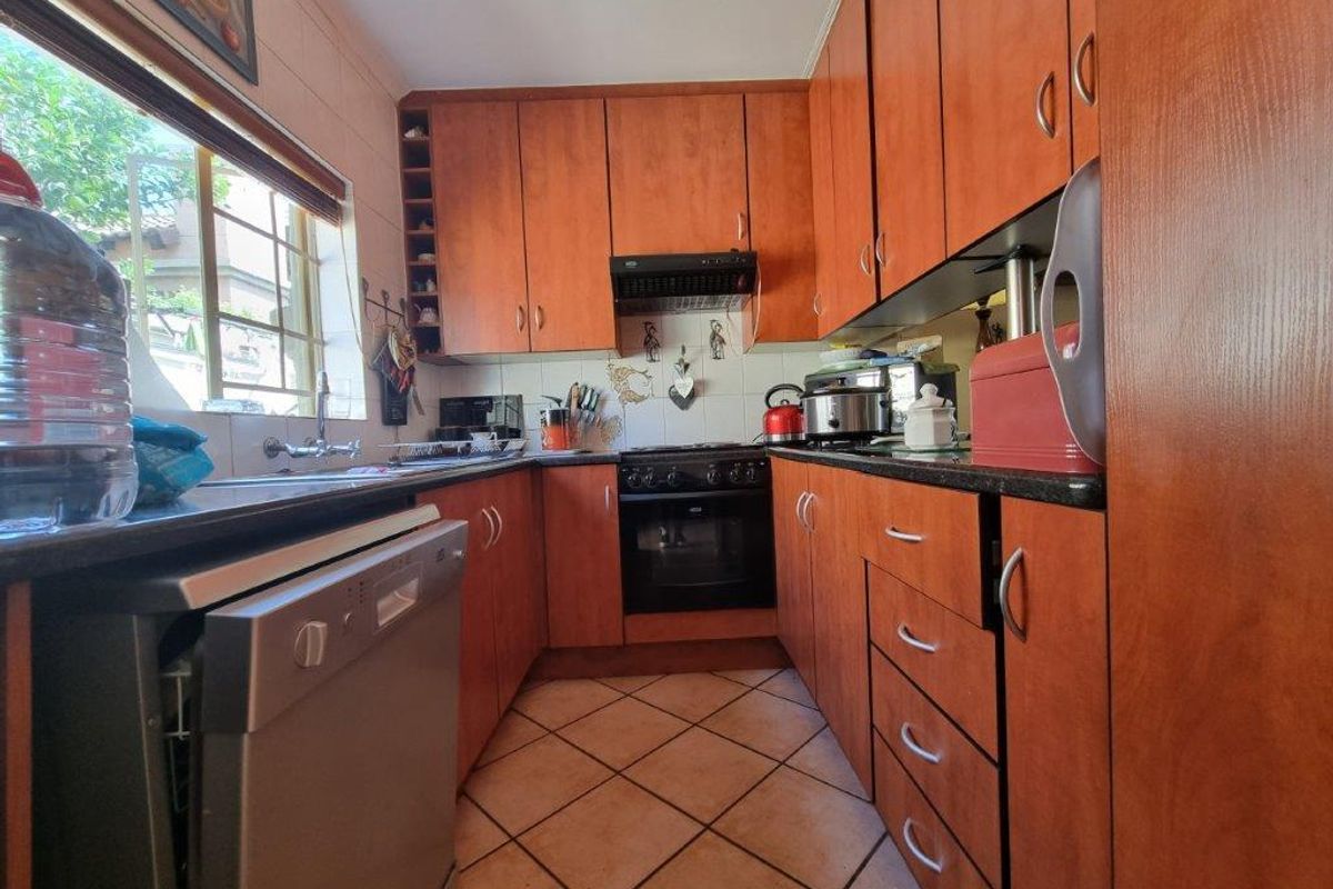A functional kitchen featuring warm-toned laminate cabinetry, granite countertops, built-in oven, extractor fan, and tiled flooring with a window overlooking the exterior.