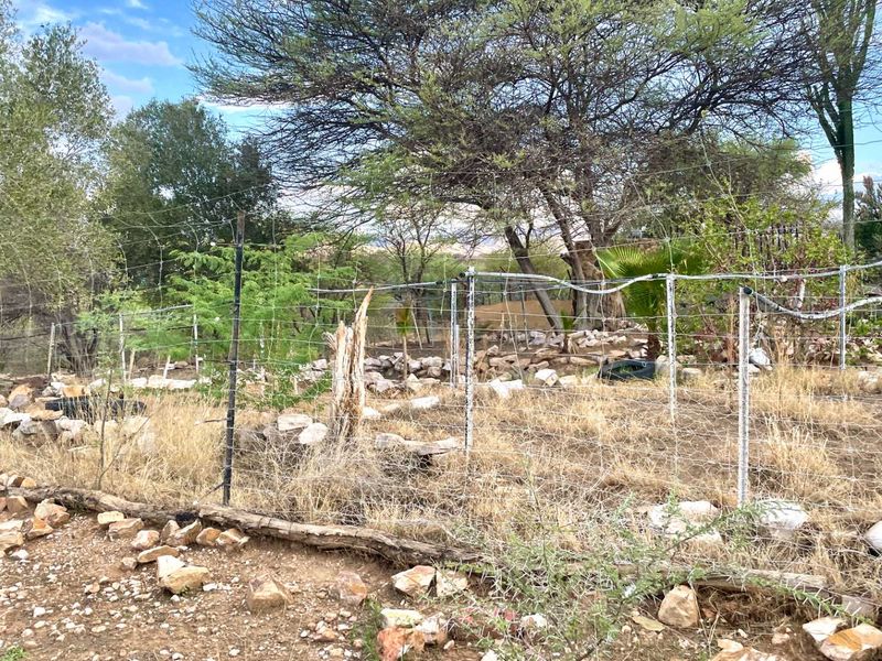 An undeveloped plot of land featuring dry vegetation, natural stone borders, and existing wire mesh perimeter fencing.