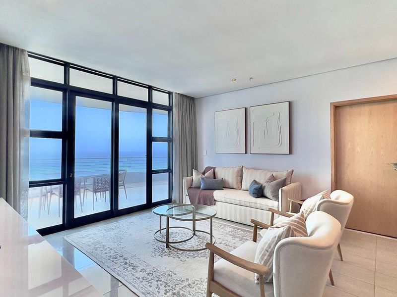 A bright and modern living room featuring large sliding glass doors that open onto a balcony with ocean views.