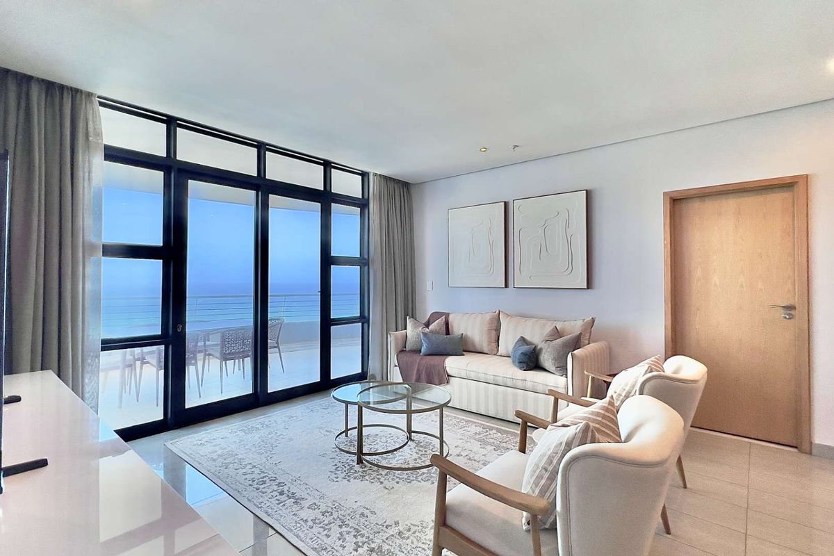 A bright and modern living room featuring large sliding glass doors that open onto a balcony with ocean views.