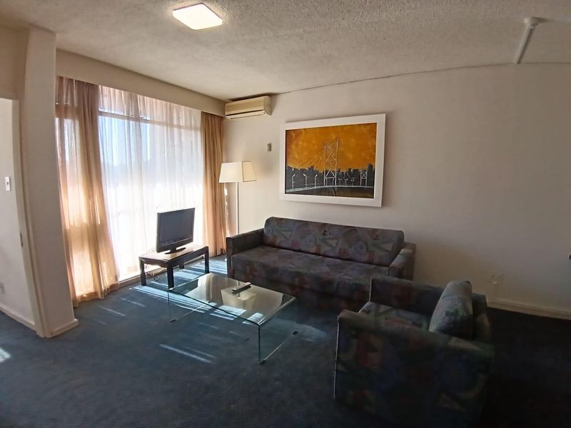 A living room featuring carpeted flooring, a large window with curtains, and a wall-mounted air conditioning unit.