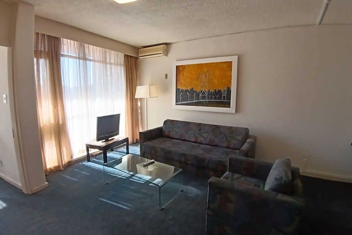 A living room featuring carpeted flooring, a large window with curtains, and a wall-mounted air conditioning unit.