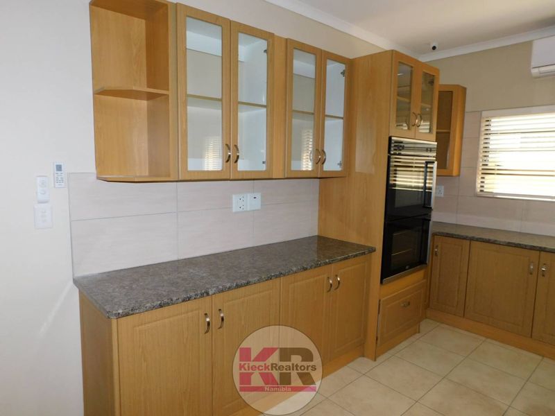 A clean, functional kitchen featuring light wood cabinetry, granite-look laminate countertops, a built-in double oven, and neutral tiled flooring.