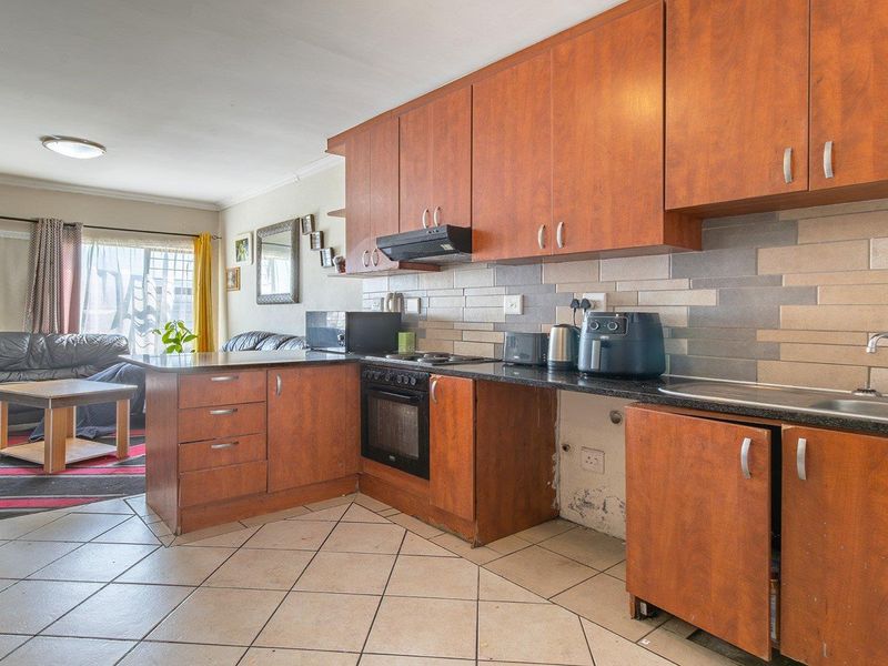 Open-plan kitchen and living area featuring wooden cabinetry, tiled flooring, and a tiled backsplash, requiring some maintenance to the lower kitchen cabinets.