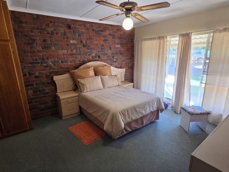 Spacious bedroom featuring an exposed brick accent wall, built-in wooden cabinetry, a ceiling fan, and direct access to the outdoors via sliding glass doors.