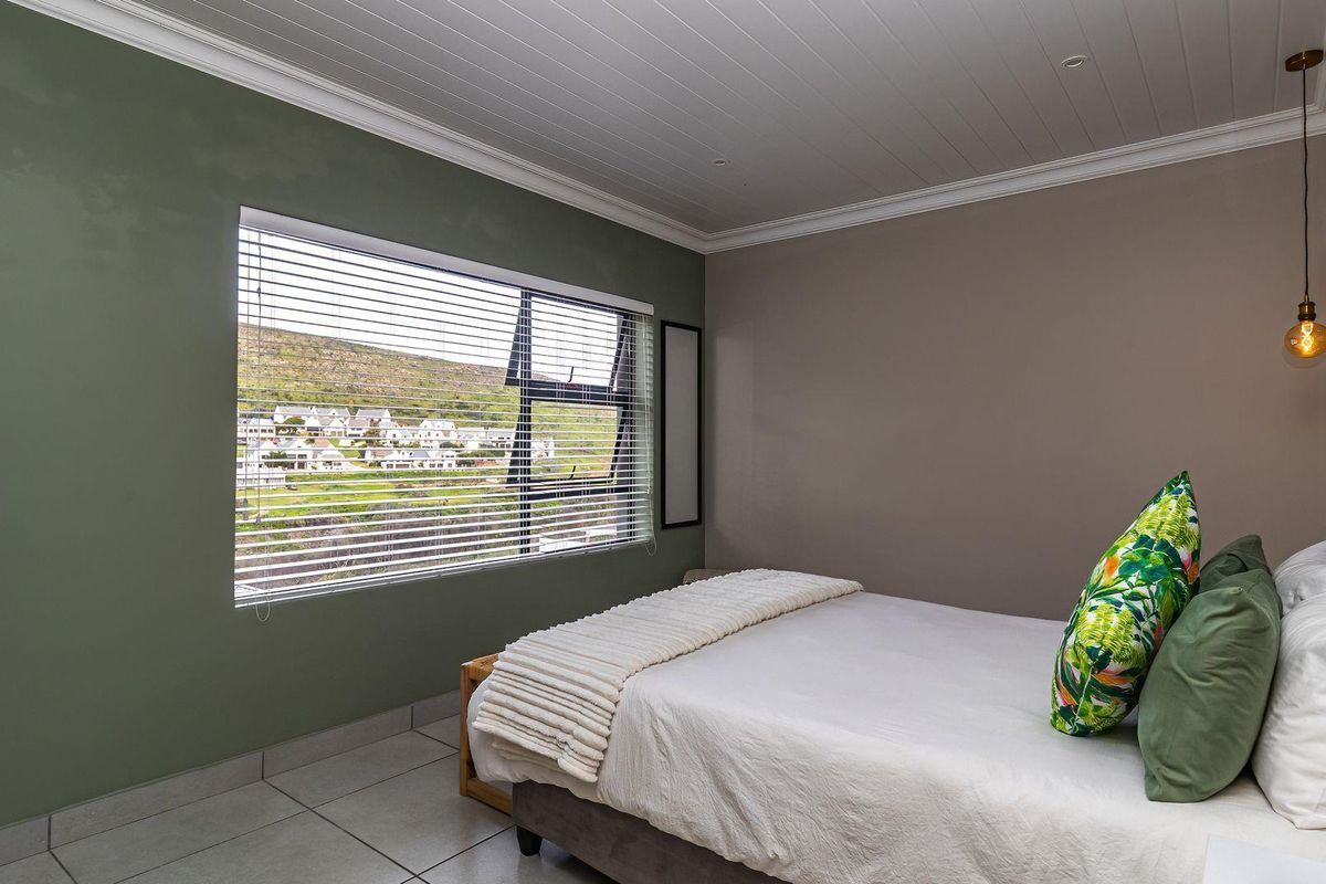 A well-maintained bedroom featuring tiled flooring, a tongue and groove ceiling with coving, and a large window with venetian blinds offering scenic views.