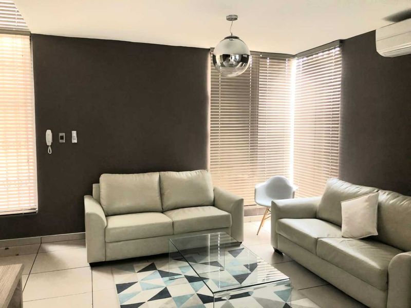 A well-lit living room featuring tiled flooring, modern venetian blinds, and a wall-mounted air conditioning unit.