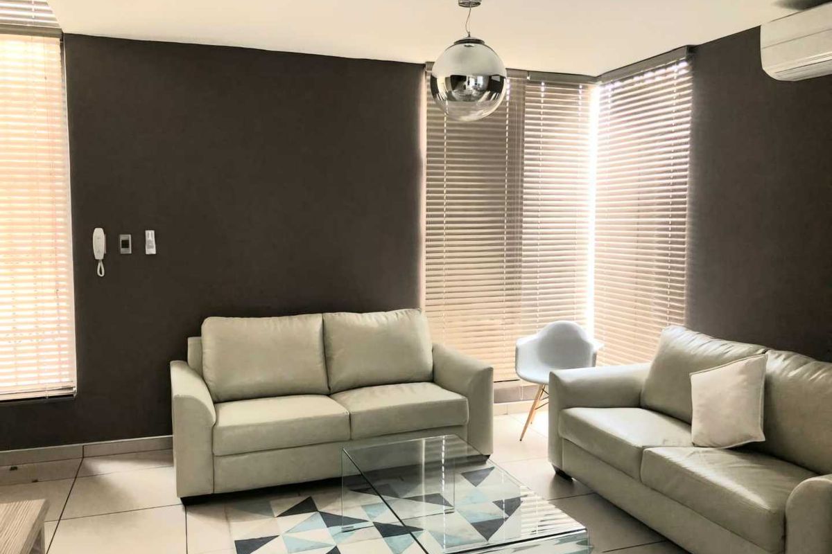 A well-lit living room featuring tiled flooring, modern venetian blinds, and a wall-mounted air conditioning unit.