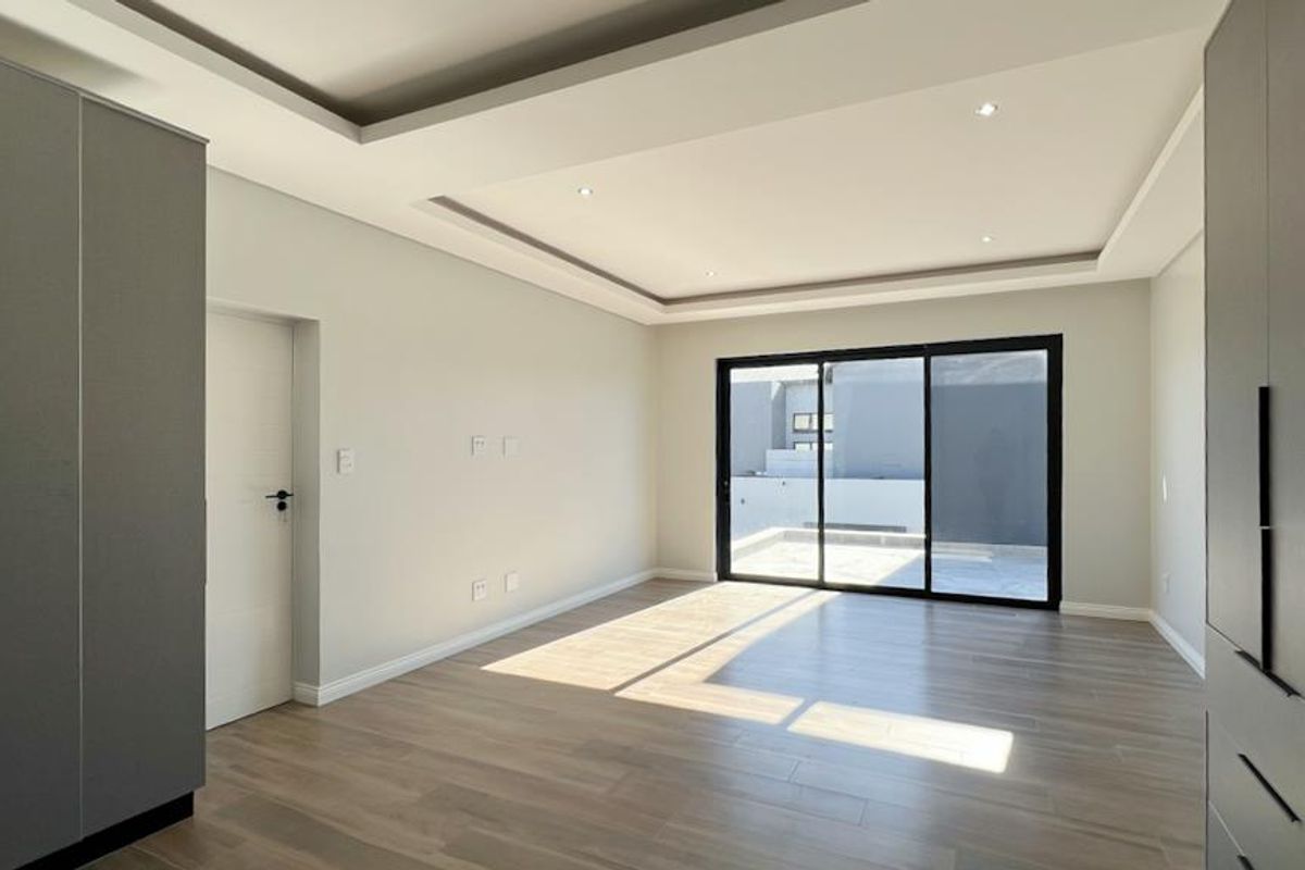 A bright, modern bedroom featuring built-in cabinetry, recessed ceiling lighting, and large sliding glass doors opening to an outdoor area.