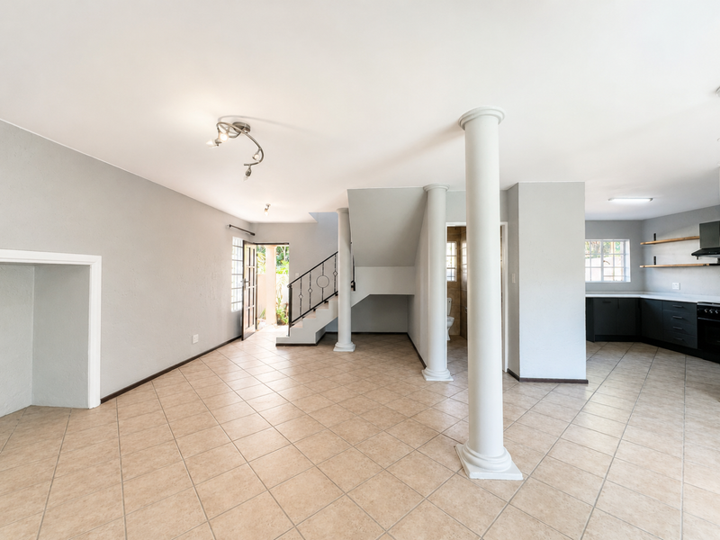 Spacious open-plan living area featuring tiled floors, decorative columns, a staircase, and a modern kitchen with built-in cabinetry and appliances.