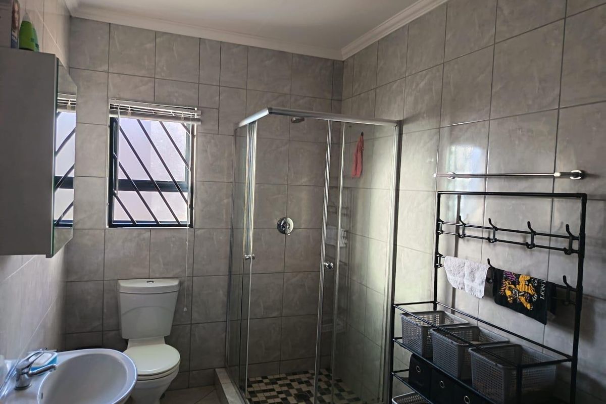 A functional bathroom featuring a glass-enclosed shower, ceramic wall tiling, a pedestal basin, and a toilet with security bars on the window.