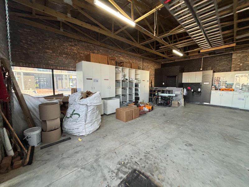 Spacious garage or utility area featuring exposed brick walls, timber roof trusses, concrete flooring, and extensive built-in storage cabinetry.