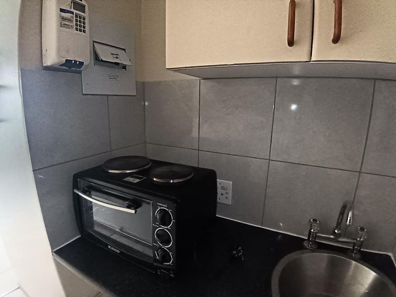 A compact kitchen area featuring built-in cabinetry, a tiled backsplash, a stainless steel sink, and a wall-mounted prepaid electricity meter.