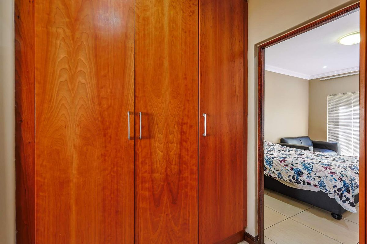 A bedroom featuring built-in wooden cupboards and tiled flooring, with a view into the adjacent sleeping area.