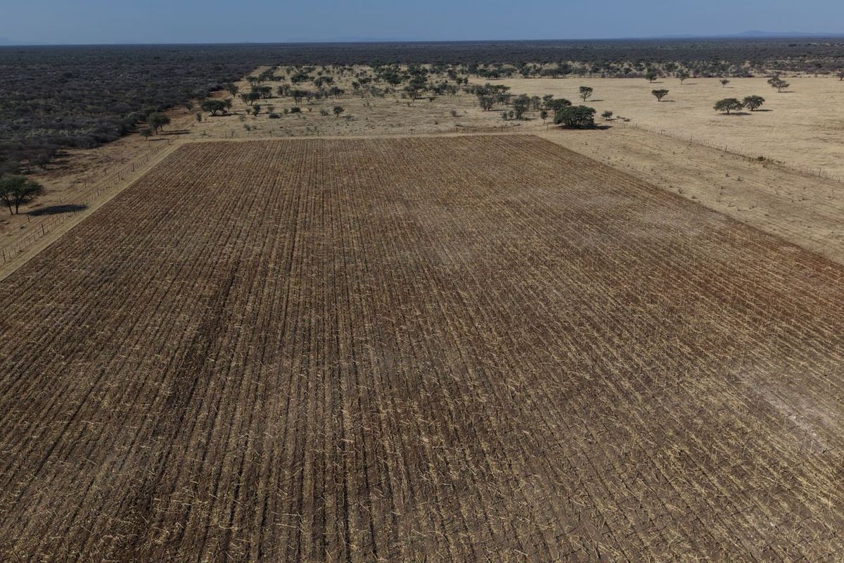 An aerial view of a large, open agricultural field on a farm, featuring clear boundary fencing and expansive dry landscape.