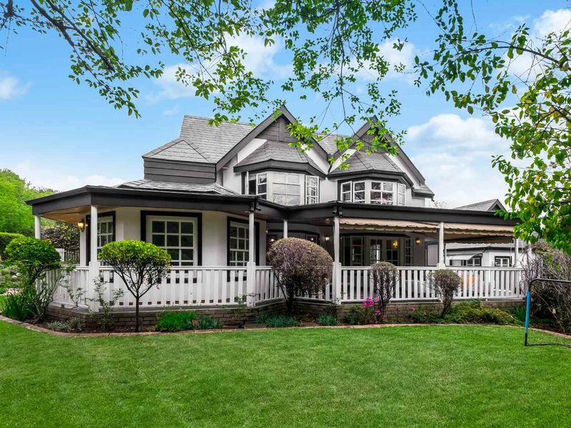 A well-maintained rear elevation featuring a spacious covered patio with a classic balustrade, overlooking a lush, manicured garden.