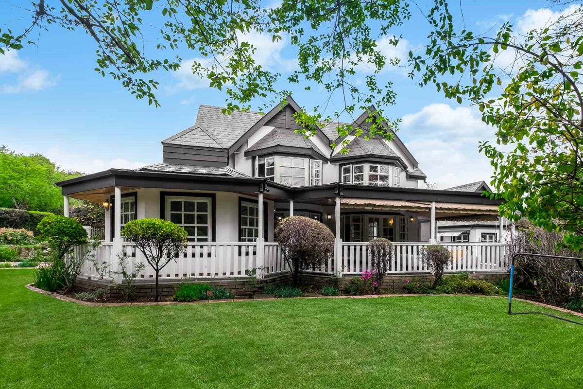 A well-maintained rear elevation featuring a spacious covered patio with a classic balustrade, overlooking a lush, manicured garden.