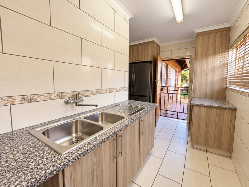 A clean and functional scullery featuring double stainless steel sinks, granite countertops, ample built-in cabinetry, and direct access to the exterior.