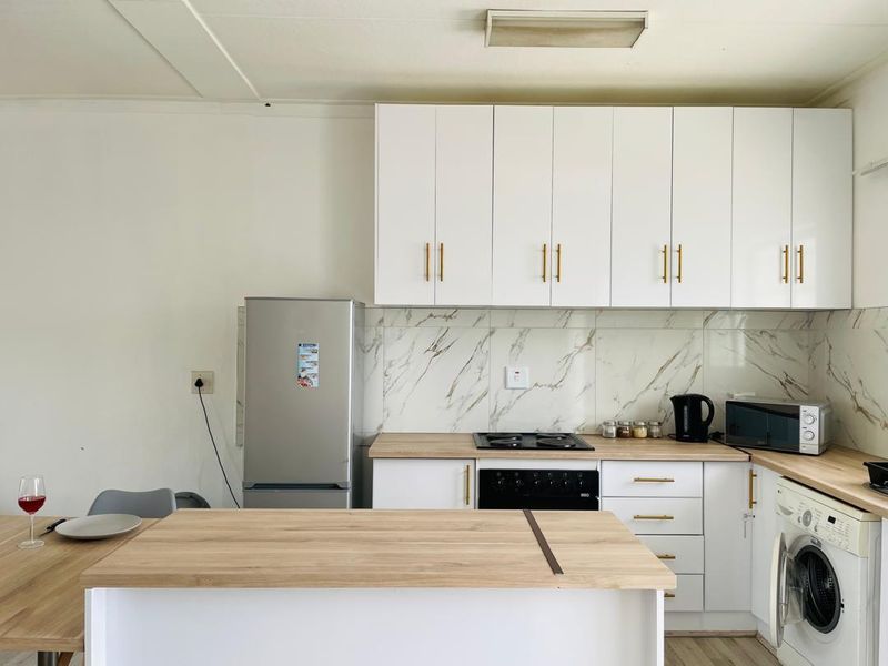 Modern kitchen featuring white cabinetry, marble-look splashback, wood-look countertops, built-in oven, electric hob, and an integrated washing machine.