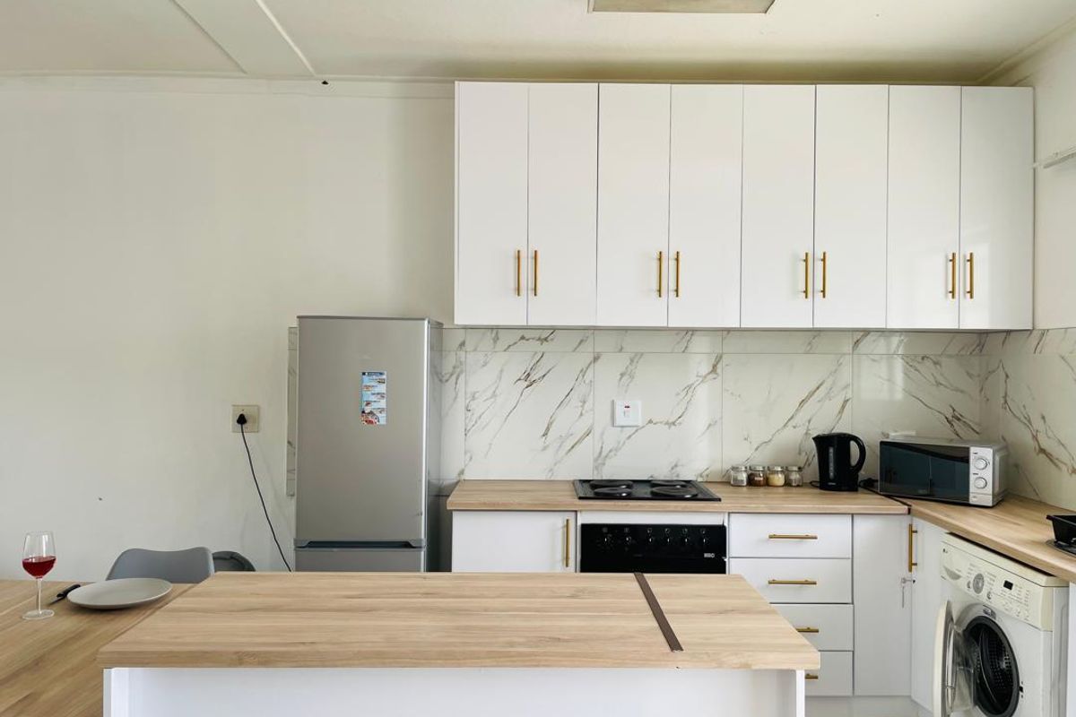 Modern kitchen featuring white cabinetry, marble-look splashback, wood-look countertops, built-in oven, electric hob, and an integrated washing machine.
