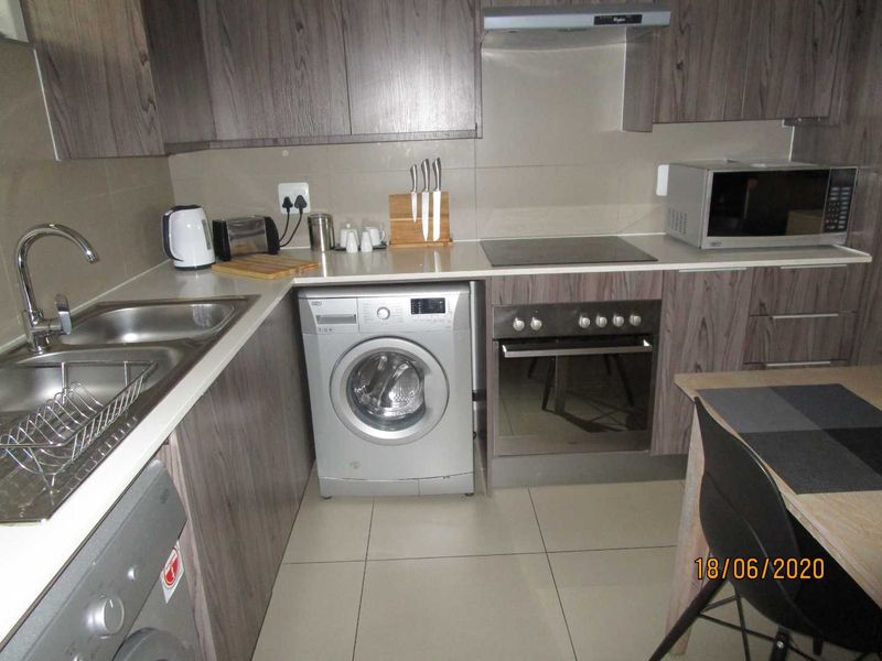 Compact kitchen featuring modern wood-grain cabinetry, integrated appliances, stainless steel sink, and tiled finishes.