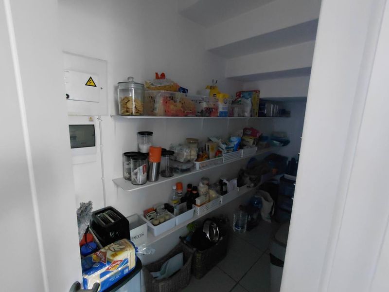 A functional walk-in pantry or scullery area featuring multiple levels of built-in shelving and an integrated electrical distribution board.
