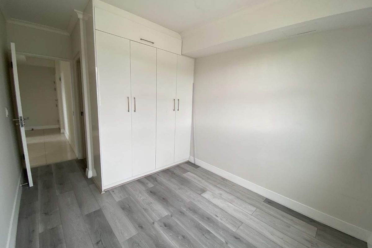 A bright, empty bedroom featuring modern grey wood-look flooring and floor-to-ceiling built-in white cabinetry.