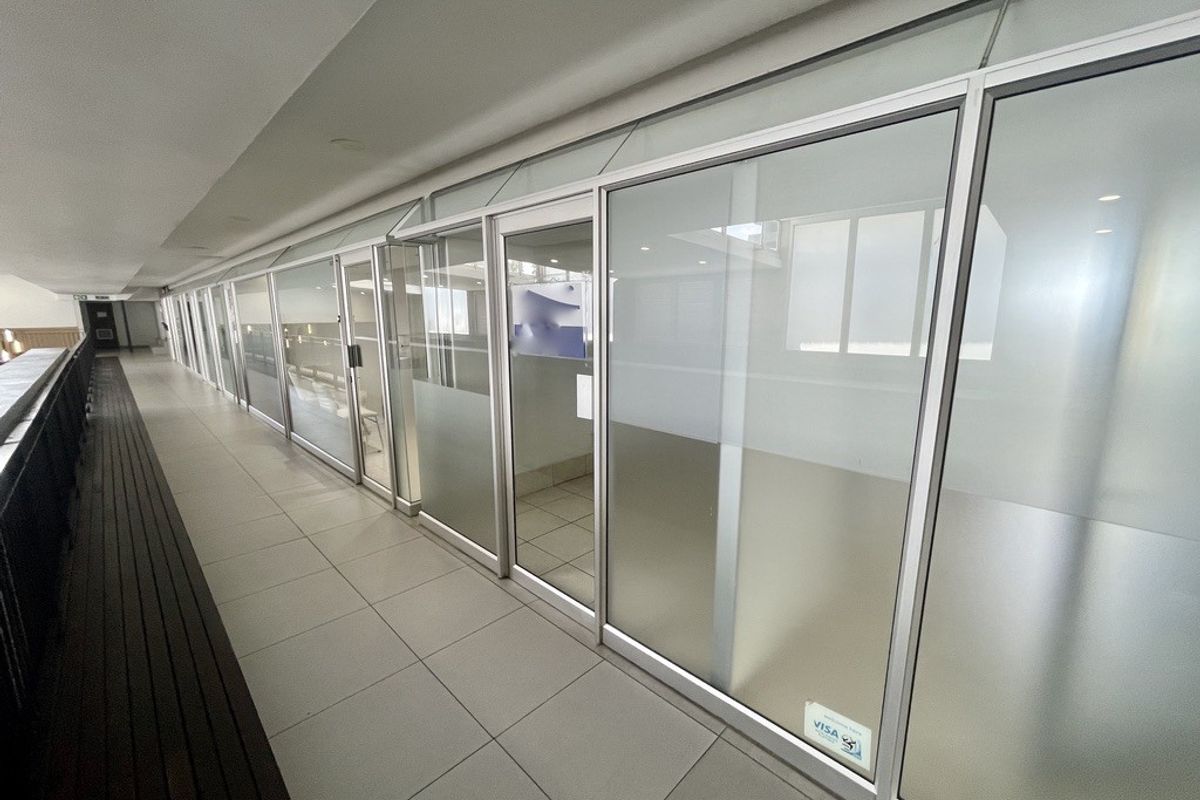 A bright, modern commercial hallway featuring extensive glass partitioning, aluminum framing, and clean tiled flooring, suitable for office or retail use.
