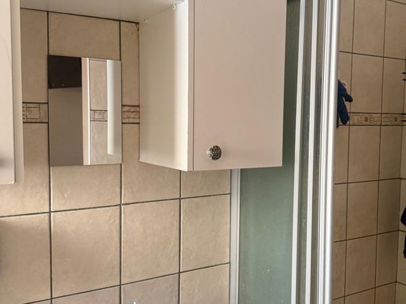A functional bathroom featuring a wall-mounted vanity cabinet, ceramic washbasin, and a shower enclosure with tiled wall finishes.