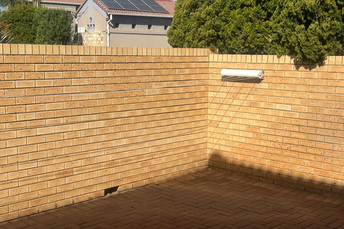 A private rear courtyard area featuring brick boundary walls, paved flooring, and a wall-mounted retractable clothesline.