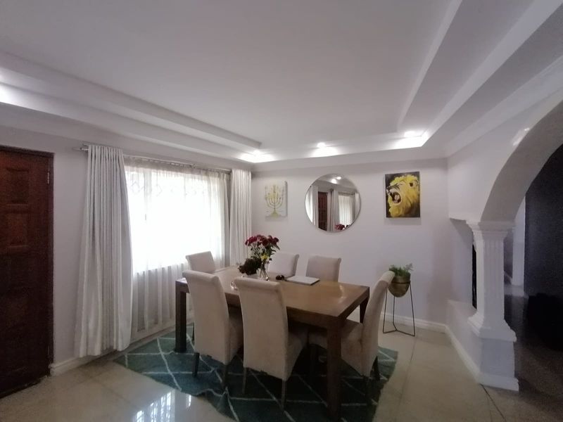 A well-lit dining room featuring a decorative archway, recessed ceiling details, and polished tile flooring, creating a bright and inviting space for meals.