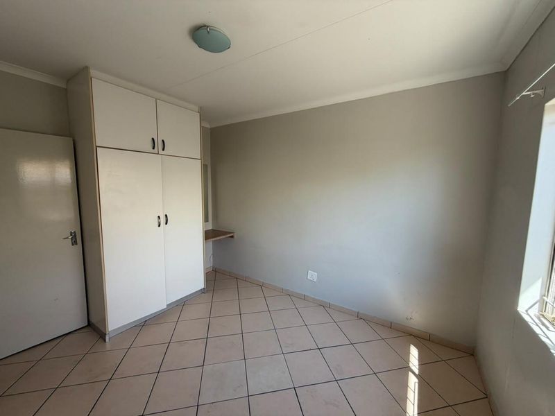 An empty bedroom featuring tiled flooring, a built-in wardrobe with an integrated vanity shelf, and neutral wall finishes.