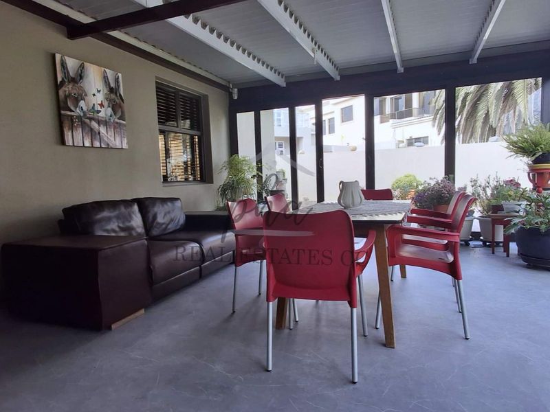 A covered patio area featuring concrete flooring, exposed beam ceiling, and large sliding glass doors providing access to the garden.