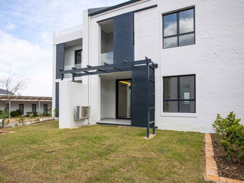Modern rear exterior view of an apartment featuring a painted brick facade, aluminium windows, and a private patio area with a pergola.